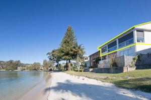 a house on the shore of a beach next to the water at Sunrise Waters 2-63 Soldiers Point Road, stunning waterfront property in Soldiers Point