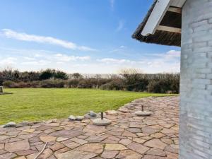 a stone patio with a grass field and a building at Holiday Home Herlek - 450m from the sea in Bornholm by Interhome in Åkirkeby