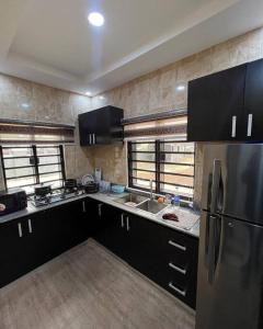 La cuisine est équipée de placards noirs et d'un réfrigérateur en acier inoxydable. dans l'établissement Enugu Airbnb / shortlet Serviced Apartment, à Enugu