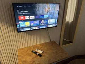 uma televisão pendurada numa parede com dois comandos remotos numa mesa em Quarto Econômico com Ar Cond. e Smart Tv Netflix em Itajaí