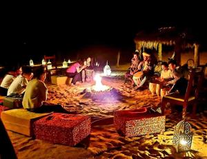 un groupe de personnes assises autour d'un foyer extérieur la nuit dans l'établissement Sahara Relax Camp, à Merzouga