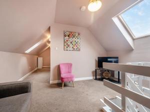 a attic living room with a pink chair and a tv at Home Farm - The Coo Shed in Dunragit