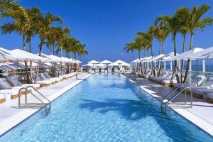 una piscina con sombrillas blancas y palmeras en Oceanview 1 Hotel & Homes 1 Bedroom 1 and Half Bathrooms Luxe Condo with Balcony, en Miami Beach