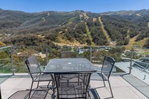 a glass table and chairs on a balcony with mountains at Lantern 1 Bedroom Balcony with Village and Mountain View in Thredbo