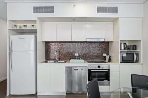 a kitchen with white cabinets and a refrigerator at Cosy 1-Bed Unit with a Gym, BBQ Area, Spa and Pool in Brisbane