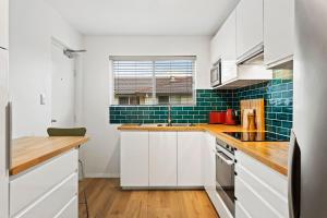 a kitchen with white cabinets and blue subway tiles at Mid-Century Morningside 2-Bed Apartment in Brisbane