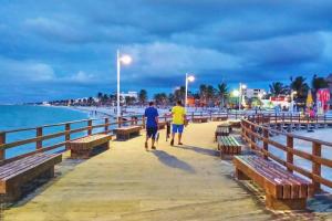 zwei Menschen, die auf einem Pier neben dem Meer laufen in der Unterkunft Cómodo Departamento a 2 cuadras de la playa in Progreso