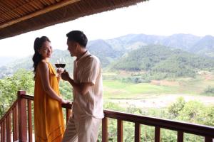 a man and woman standing on a balcony with a glass of wine at Le Champ Tu Le Resort Hot Spring & Spa in Yen Bai