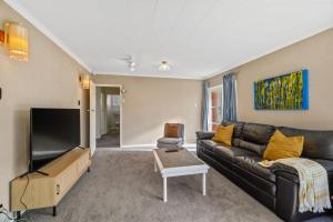 a living room with a black leather couch and a flat screen tv at Red Brick Cottage-First choice for families in Rotorua