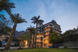 a building with palm trees in front of it at Tripli Hotels Ayushman Retreat in Rishīkesh