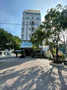 a large white building with a tree in front of it at Hồng Nhung Hotel Kiên Giang in Rạch Giá