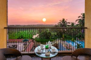 a balcony with a table and chairs and a sunset at Golden Tulip Candolim, Goa in Candolim