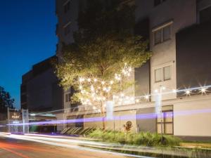 Clef Hotel Bangkok في بان كلونغ سامرونغ: شجرة على جانب مبنى به أضواء