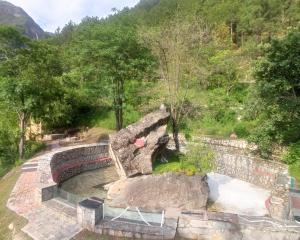 a stone bridge over a pond in a park at Mashoo Resorts , Bhuntar in Shamshi
