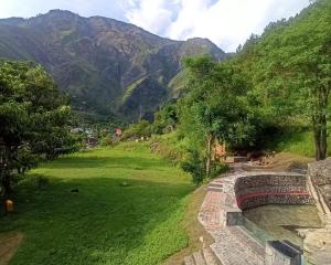 a view of a green field with mountains in the background at Mashoo Resorts , Bhuntar in Shamshi