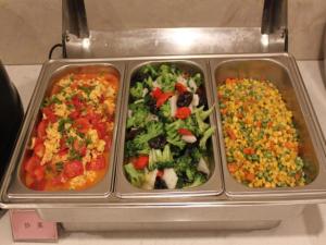 three metal trays of food with broccoli and other vegetables at GreenTree Inn Yancheng Tinghu Area Wengang Road New Fourth Army Memorial Hotel in Yancheng