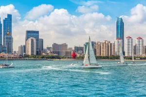 three sailboats in the water in front of a city at Metropolo Hotel Qingdao Wusi Square Xiaomaidao in Qingdao