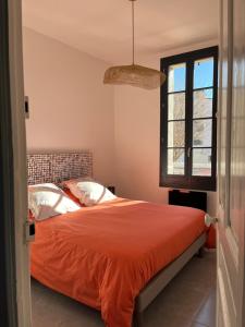 a bedroom with a bed with an orange comforter and a window at Quai du Félibre in LʼIsle-sur-la-Sorgue