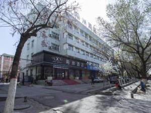 duży biały budynek przy ulicy miejskiej z drzewami w obiekcie Xana Hotelle Shihezi Junken Museum Branch w mieście Shihezi