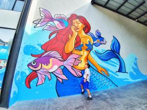 a boy standing in front of a mural of a mermaid at The Bed Vacation Rajamangala Hotel in Songkhla