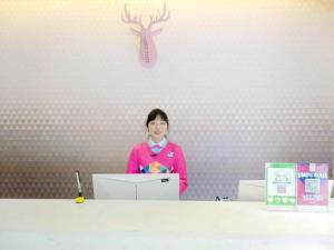 a woman standing behind a counter with a pink wall at PAI Hotels·Kangding Xiaqiao in Garze