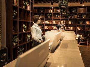 une femme debout dans une bibliothèque à la recherche de livres dans l'établissement James Joyce Coffetel·Chengde Mountain Resort Toudao Pailou, à Chengde