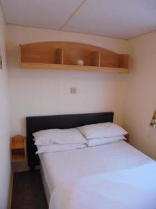 a small bedroom with a bed and a shelf at 6 berth 3 bedroom Northshore Skegness Emirates in Skegness