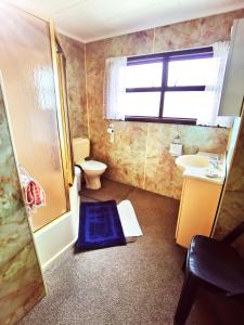 a bathroom with a toilet and a sink and a window at Denby Golf House Tikipunga in Whangarei