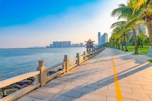 a walkway next to the water with palm trees at Thank Inn Plus Hotel Zhuhai Nanping pedestrian Street Huafa shopping Center in Zhuhai