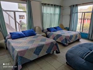 2 Betten mit blauen Kissen in einem Zimmer mit Fenstern in der Unterkunft Luz del Mar Paredón in El Paredón Buena Vista