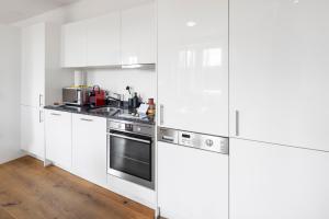 una cocina blanca con electrodomésticos de acero inoxidable y armarios blancos en STAYY The River - contactless check-in, en Zúrich