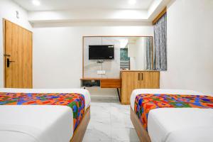 two beds in a room with a tv and a mirror at FabHotel Amantra in Ahmedabad