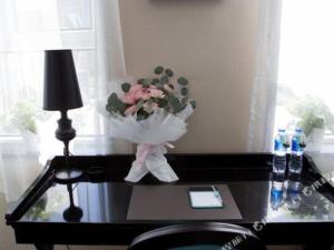 uma mesa com um vaso de flores e um comprimido em Xana Hotelle Ulanqab Municipal Government Wanda Plaza em Jining