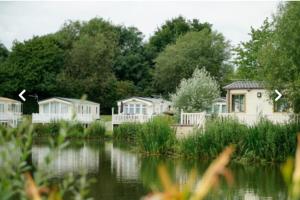 a row of houses next to a body of water at Bumble Bee Lodge, Hoburne Cotswold Holiday Park in South Cerney