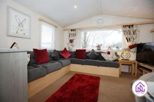 a living room with a gray couch with red pillows at Bumble Bee Lodge, Hoburne Cotswold Holiday Park in South Cerney