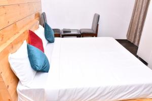 Un dormitorio con una cama blanca con almohadas azules y rojas en Hotel The Crown, Dharamshala, en Dharamshala