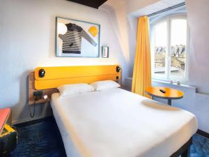 ibis Styles Saint Malo Centre Historique في سان مالو: غرفة نوم بسرير مع اللوح الأمامي الأصفر ونافذة
