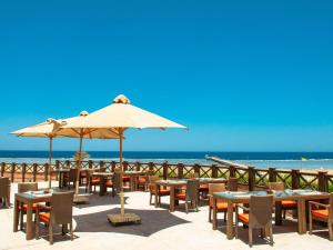 einen Strand mit Tischen, Stühlen und einem Sonnenschirm in der Unterkunft Novotel Marsa Alam Beach Resort in Al-Qusair