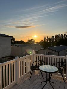 a table and chairs on a deck with the sunset at Escape City Caravan in Lytchett Minster