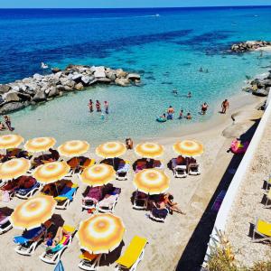 a beach with chairs and umbrellas and people in the water at Hotel resort Rocca di Vadaro in Capo Vaticano