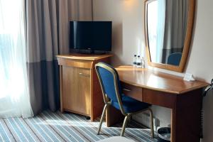 um quarto com uma secretária, uma televisão e um espelho em Colnbrook Hotel London Heathrow Airport em Hillingdon