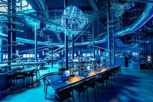 - un groupe de tables et de chaises dans une pièce aux lumières bleues dans l'établissement Hôtel Station Cosmos, à Chasseneuil-du-Poitou