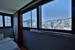 a bedroom with two windows and a view of a city at Hermes Hotel in Busan