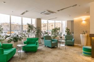 una sala de espera con sillas verdes, mesas y ventanas en Elements Kirov Hotel, en Kirov