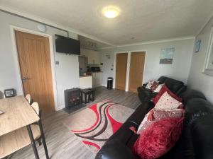 a living room with a black leather couch and a kitchen at 246, Belle Aire, Hemsby - Beautifully presented two bed chalet, sleeps 5, pet friendly, close to beach! in Great Yarmouth