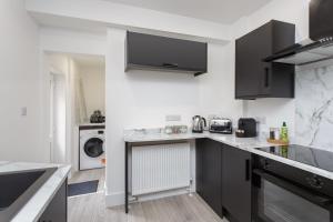 een keuken met grijze kasten en een wasmachine en droger bij Henderson Lodge - Cosy, modern 3 bed 2 bath house in Portsmouth