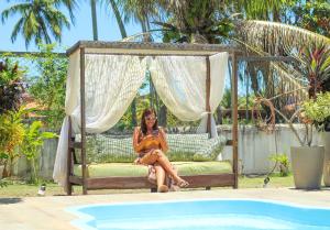 Pousada Iandê Patacho في بورتو دي بيدراس: امرأة تجلس على مرجيحة بجوار حمام سباحة