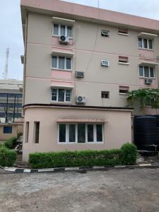 un bâtiment rose avec des fenêtres et des buissons devant lui dans l'établissement GREEK VIEW APARTMENT VICTORIA ISLAND, à Lagos