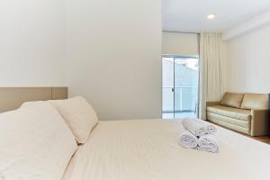 a bedroom with a white bed with two towels on it at VC 106 - FLAT VILA DO CENTRO in Bombinhas