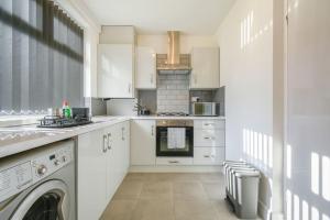 a kitchen with white cabinets and a washer and dryer at Modern Home: Heart Of Blackburn in Blackburn